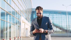 Attractive businessman walks by the airport, gets the message, uses the phone, is surprised with the result, reacts happily to it. Being a winner, happy emotions. True emotions. - Powered by Shutterstock - Get 15% off with code: PIKWIZARD15