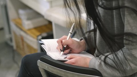 Female hands quickly write text in a notebook. Lesson on eyebrow correction or makeup. Young brunette woman taking notes. Close-up of shot.