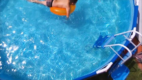 Little Boy Swimming In Pool on orange inflatable rubber ring. 