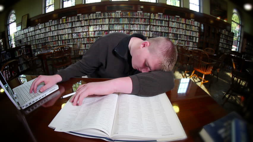 A tired male student sleeps in the library.