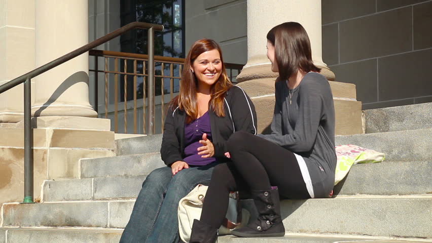 Students walk and socialize on the steps of the college library.