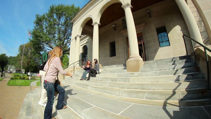 Students walk and socialize on the steps of the college library.