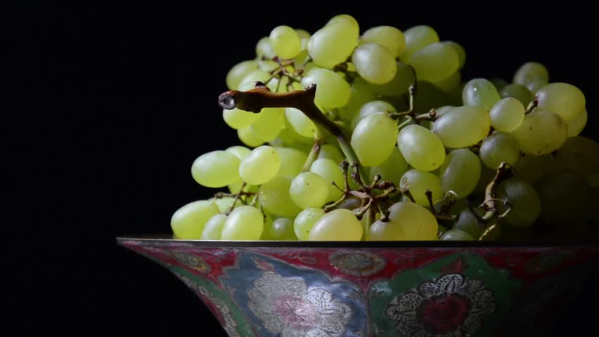 White grapes on an old painted bowl on a black background. (Rotating)