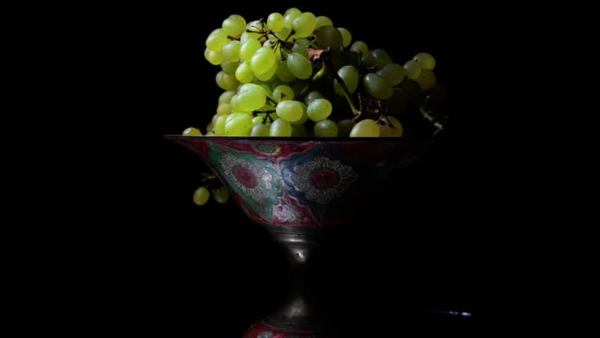 White grapes on an old painted bowl on a black background. (Rotating)
