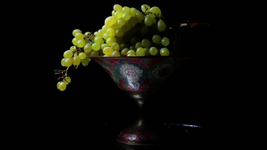 White grapes on an old painted bowl on a black background with a glass of wine.