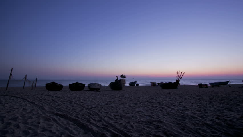 Time lapse of boats on a beach during sunrise