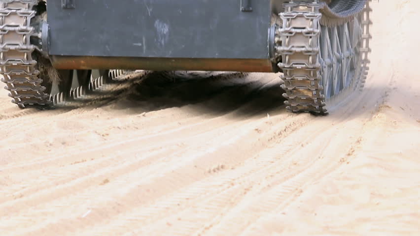 A tank of the second world war rides across the sand.