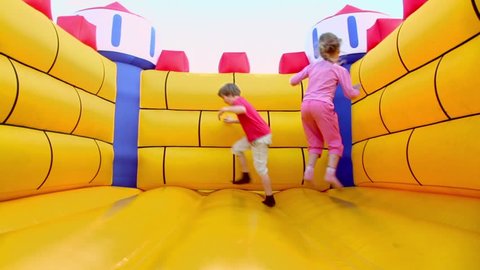 Pair of children boy and little girl jump at inflatable playground at sunny summer day
