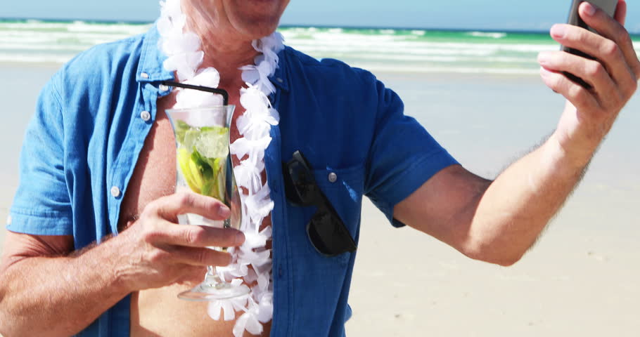 Senior man having video call on the mobile phone at the beach on a sunny day