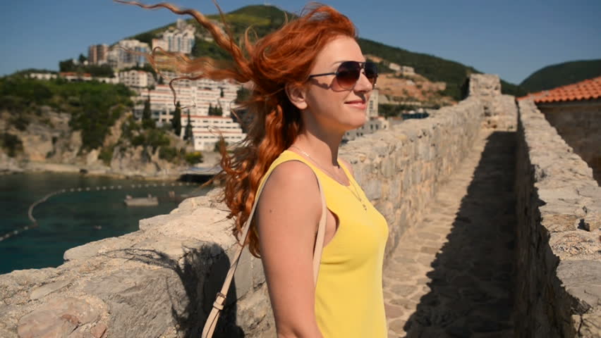 A young woman in glasses and a hat walks through an ancient city on the Adriatic coast, slow motion.