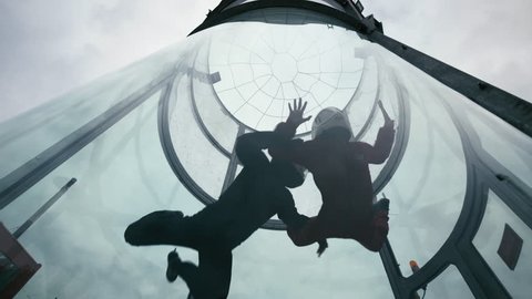 Two skydivers fly into wind tunnel. Two skydivers doing skydiving in an indoor skydiving wind tunnel. Man and woman skydivers skydiving tandem in an indoor arena