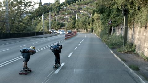 Two skateboarders speeding down a street in Stuttgart with traffic on opposing lane. Tracking shot. 