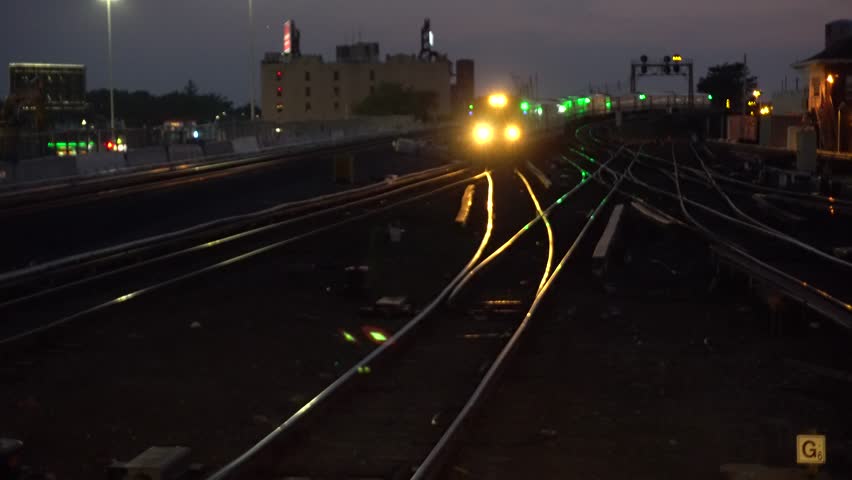 Passenger commuter train arriving at railroad station night time exterior outside video. Bright headlights illuminate track.