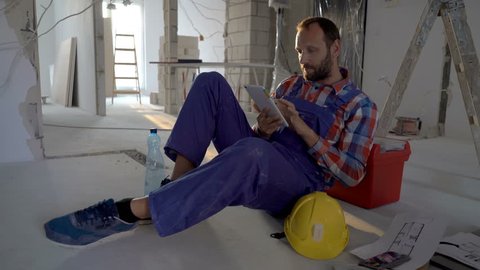 Worker sitting on the floor in his new flat and using tablet, steadycam shot
