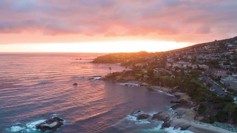 4K aerial sunset time-lapse footage over the ocean shot from the drone in Laguna Beach in California showing coastal homes, beach houses, mountains and the Pacific ocean waves.