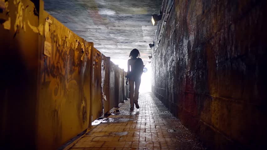 Silhouette of a slender girl in a dirty city tunnel across the road.