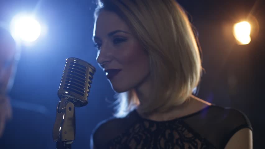 Pretty young woman, jazz singer with microphone. Shallow depth of field. Person smokes in left corner of frame