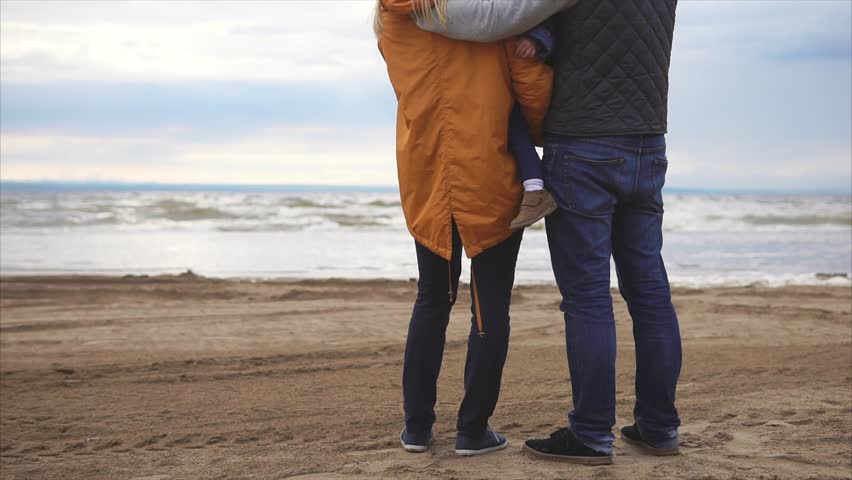 Happy young family. Man with woman and little girl standing on the ocean shore and lookin on horizont