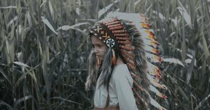 Little girl playing in a teepee tent outdoors, wearing Indian headdress, pretending to be a native American. 4K UHD RAW edited footage