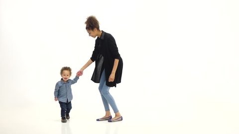 Kid holds his mother's hand and dances with her. White background. Slow motion