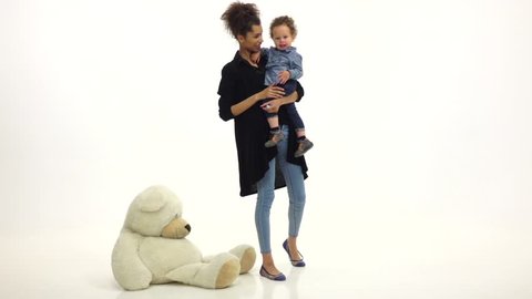 Mom african american keeps the baby and on the floor a toy bear. White background. Slow motion