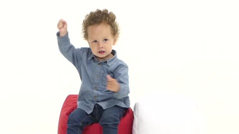 Baby of an african american is sitting on a pillow and is dancing. White background. Slow motion
