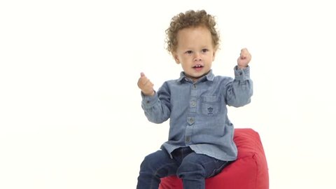 Child of an african american is sitting on a pillow and is dancing. White background. Slow motion
