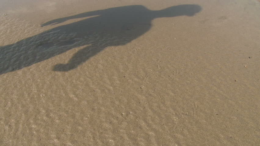 Person walks by camera leaving footprint in sand.