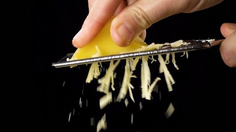 Woman hand rubbing the cheese on metal grater isolated on black background, slow motion