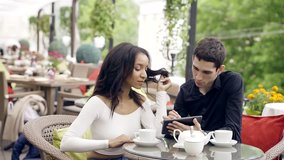 Family multi racial couple relaxing in an expensive restaurant on the veranda with a profusion of flowers and greenery. A man shows his woman the information on the screen of the computer tablet. - Powered by Shutterstock - Get 15% off with code: PIKWIZARD15