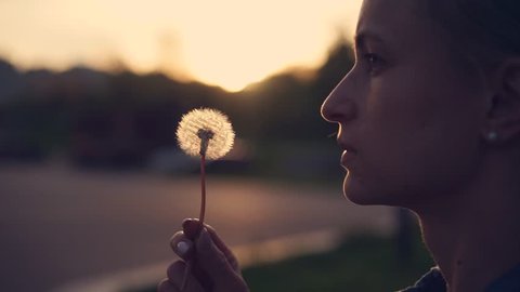 girl blowing on a dandelion at sunset