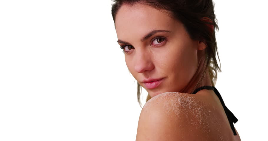 Close up of attractive Caucasian millennial looking over shoulder at camera on white background with copyspace. Closeup of beautiful young woman in string bikini with sand on shoulder in studio. 4k