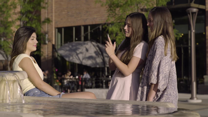 Group Of Multiethnic Friends Enjoy Sightseeing, Teen Takes Photo Of Her Friend Sitting By A Fountain 
