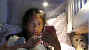 A cute little Asian girl enjoys spending time in her home made fort in her bedroom reading and using her device and hanging out with her puppy. 