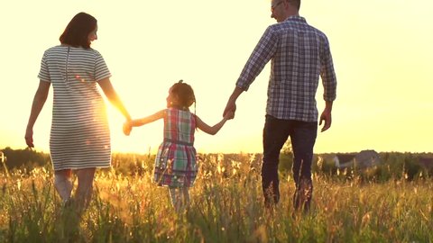 Happy Young Family with child walking on summer field. Healthy mother, father and little daughter girl enjoying nature together, outdoors. Sunset. Slow motion. 4K UHD video 3840X2160