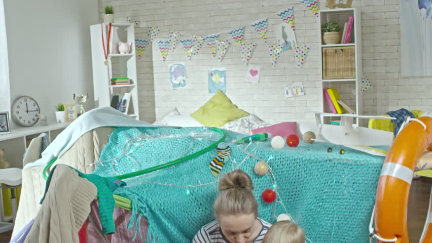 Tilt down of mother, father and two little sons sitting on the floor in living room under handmade play tent and forming colorful play dough together