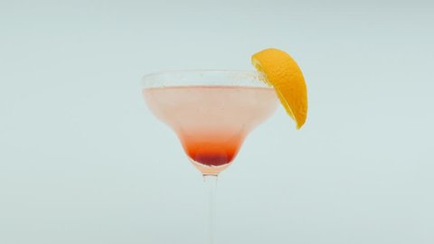 frozen margarita alcohol cocktail in glass with orange slice on light blue background, rotating 360 degrees, 4k