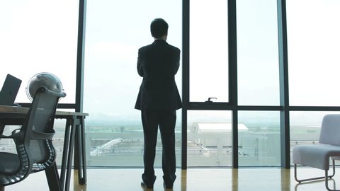 businessman standing in front of windows looking into distance