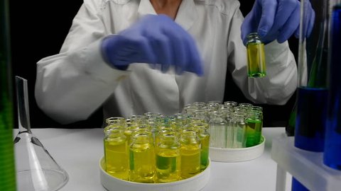 Young beautiful female scientist doing research in laboratory mixing chemical liquid blue yellow green in glass flasks black background closeup