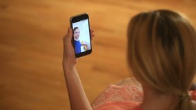 A woman is holding a video chat with a man on a smartphone. They talk fun and laugh