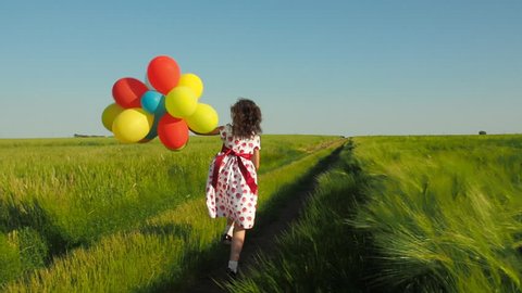 The child is running with balloons. Little girl with balloons on nature.