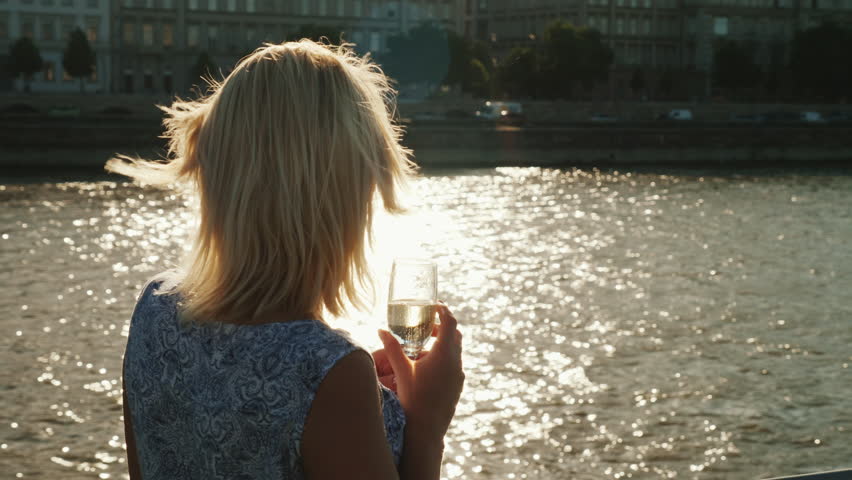 A woman with a glass in her hand admires the scenery. View from the back. Boats on the ship - a river cruise on the Danube