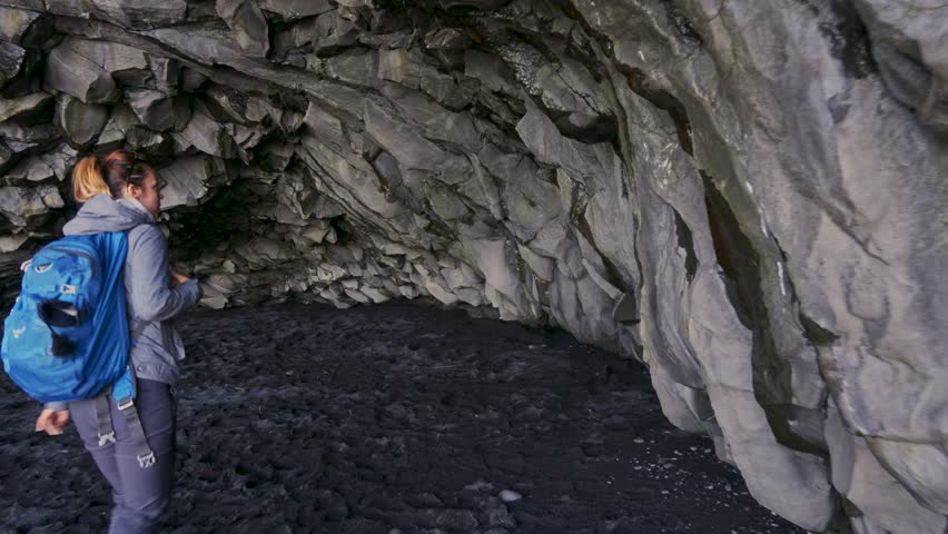 Woman exploring cave on Reynisfjara beach near Vik, Icealnd