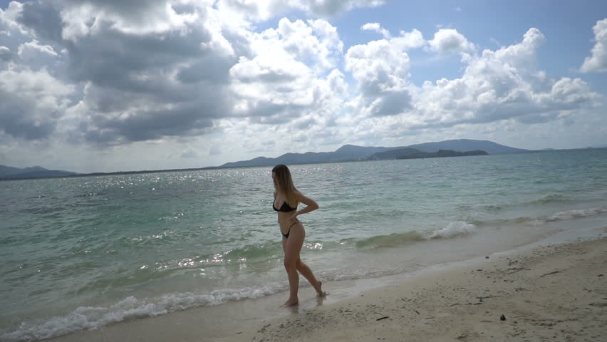 Pretty happy woman in black bikini relaxing on the sandy beach on tropical paradise island with beautiful sea and summer sky - video in slow motion