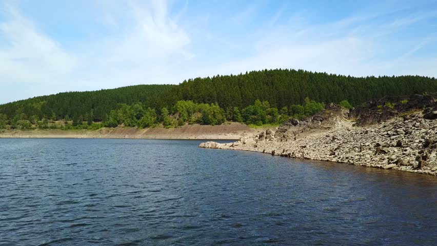 Drone video in 4k uhd format with a lake between mountains with green trees and blue sky with some white clouds and a bridge crossing the lake in the national park hart, germany.