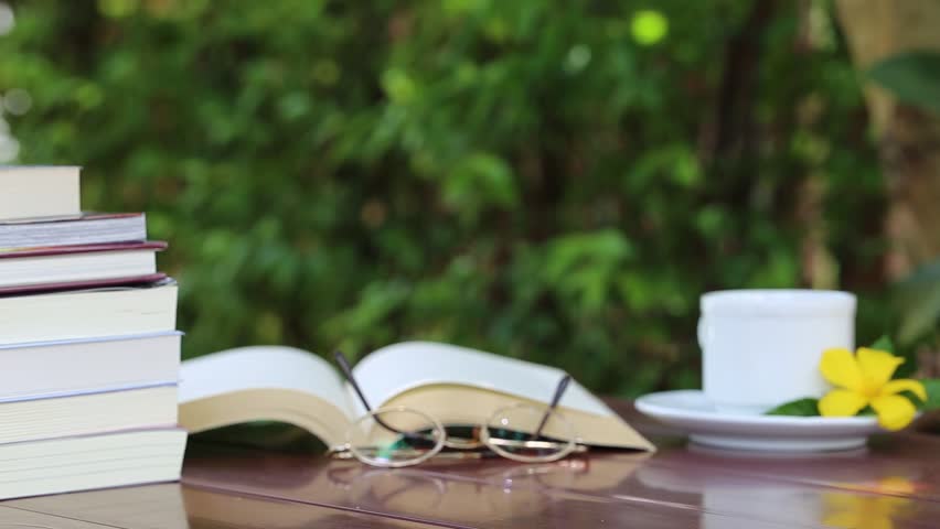 Open book and white coffee cup on table and fresh nature green garden background