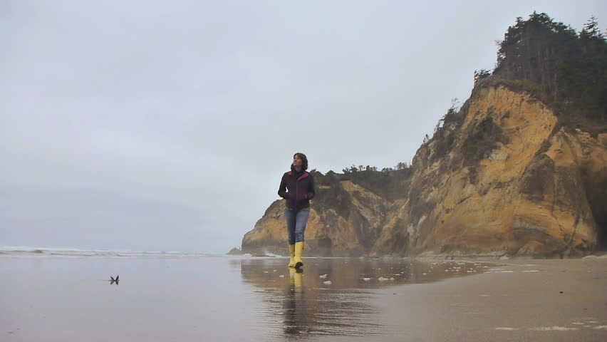 Model released woman walking by ocean on sandy, Oregon beach.