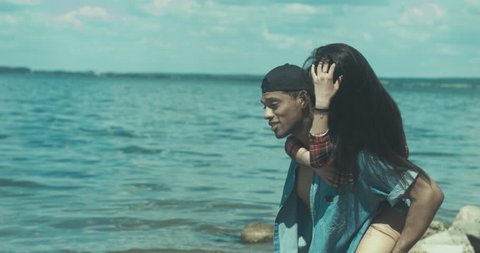 Young adult interracial couple on a beach, Caucasian female and African American man in casual clothes enjoying summer day on a sea shore. 4K UHD 60 FPS SLO MO