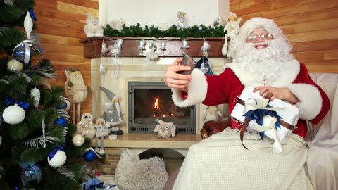 santa making selfie with smart phone, posing with christmas gift, use electronic device
