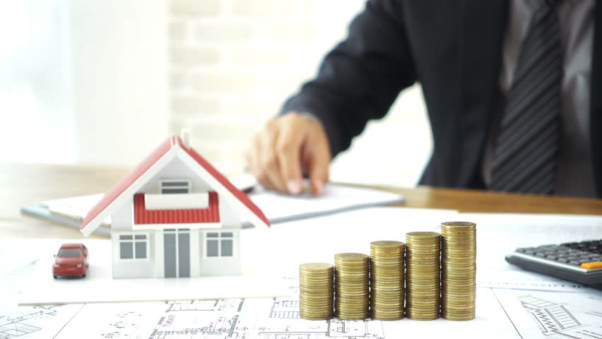 Businessman putting coin on top of money stacks with blurred house model in background - real estate financial and investment concepts Royalty-Free Stock Footage #28047895
